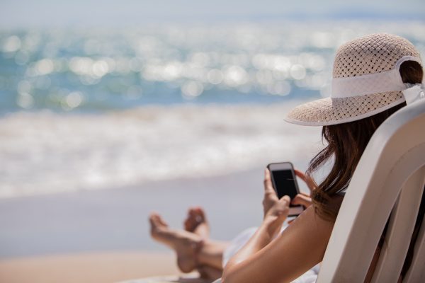 Young woman updating her social network status while relaxing at the beach